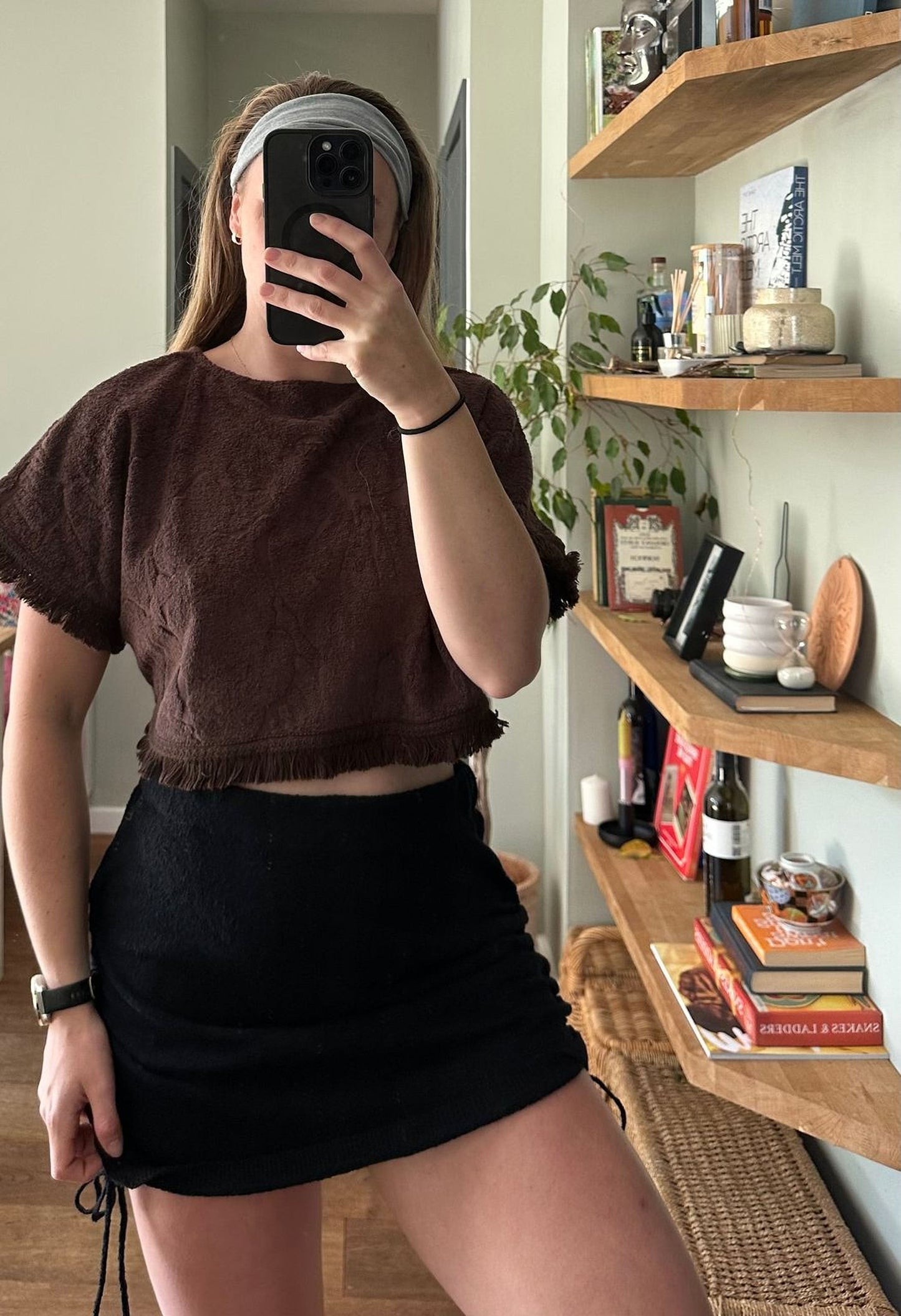 A person is taking a selfie in a room with shelves and various items, including books and decorative objects.